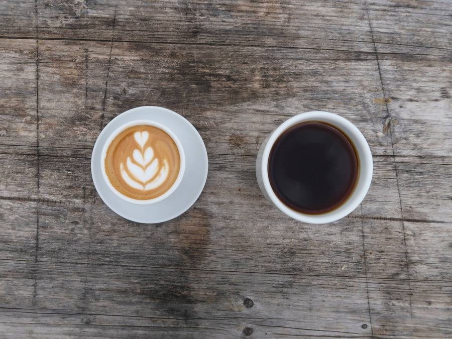 A latte with rosetta art beside a cup of black coffee