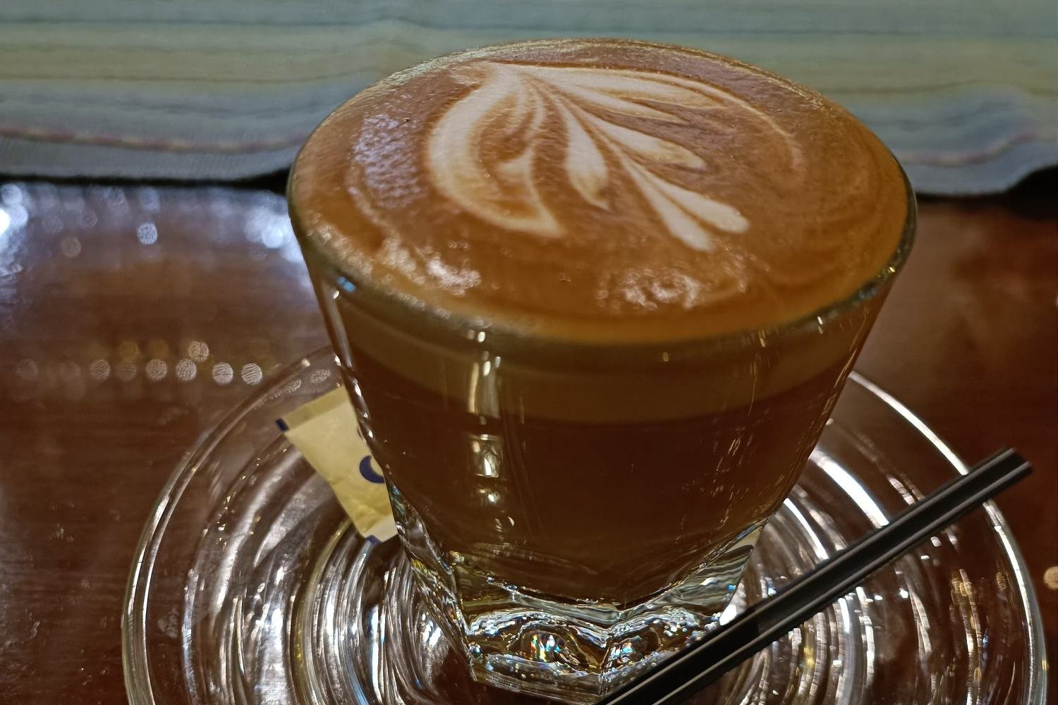 A cortado with leaf latte art in a glass on a saucer