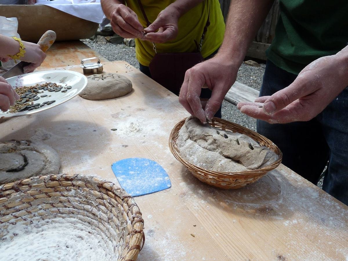 Flour-dusted hands pressing seeds into a loaf of dough
